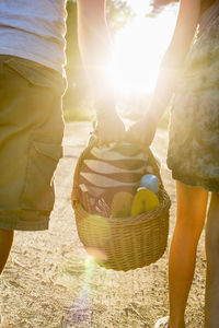 Midsection of couple carrying picnic basket against bright sun