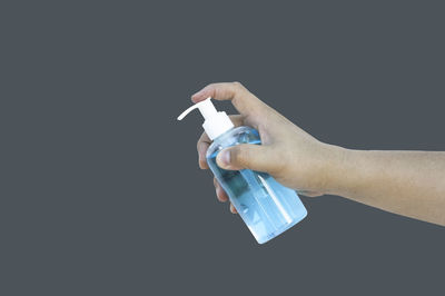 Close-up of hand holding bottle against black background