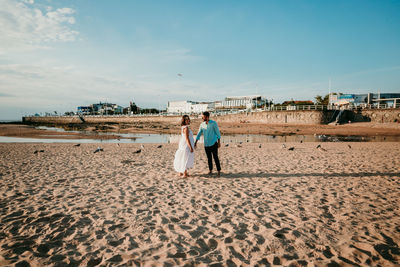 Full length of couple embracing while standing on beach against sky