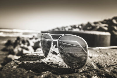Close-up of sunglasses on rock with sea reflection against sky