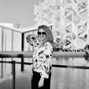 A lady wearing sunglasses standing by railing against water