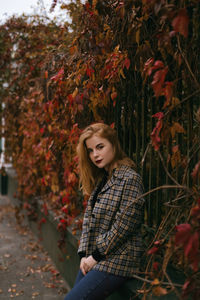Portrait of young woman standing by leaves during autumn