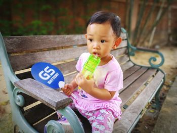 Cute baby girl drinking water while sitting on bench