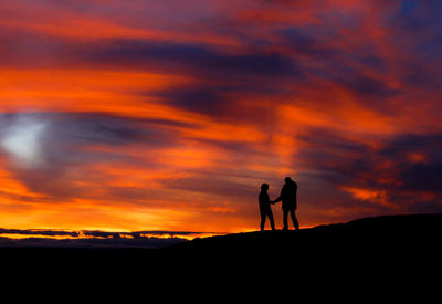 Silhouette men against dramatic sky during sunset