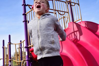 Low angle view of playful boy screaming while standing at playground