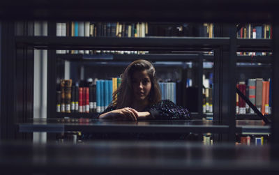 Portrait of young woman seen through bookshelves at library
