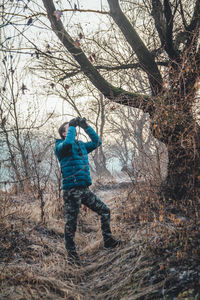 Man standing by bare tree on field