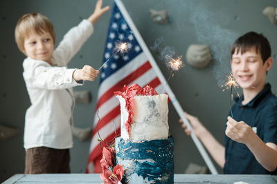 Smiling kids holding american flag and lighted sparklers at independence day celebration