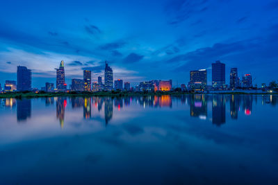 Reflection of illuminated buildings in lake against sky at dusk