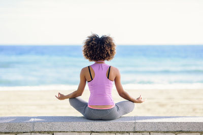 Rear view of woman meditating on retaining wall at beach