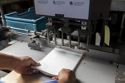 Male employee adjusting bunch of papers in print machine at shop