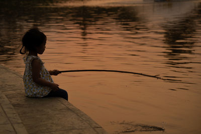 Silhouette of a young beautiful girl sitting near the pond