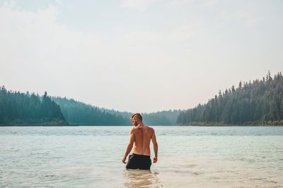 Full length of shirtless man standing in water against sky
