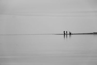 Silhouette people standing in sea against clear sky