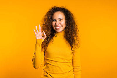 Portrait of a smiling young woman against yellow background