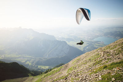 View of man paragliding over landscape against sky