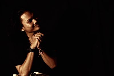 Close-up of young woman sitting against black background