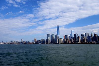Sea and buildings in city against cloudy sky