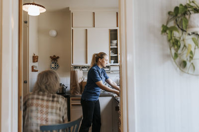 Side view of female care assistant working in kitchen at home