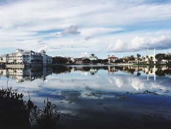 Reflection of buildings in lake against cloudy sky