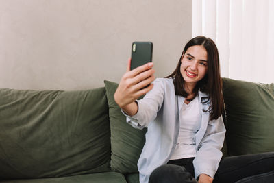 Young woman using mobile phone while sitting on sofa at home