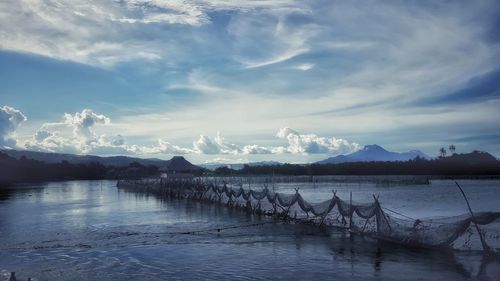 Fishing nets hanging over lake against cloudy sky