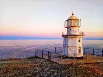 Lighthouse by sea against sky during sunset