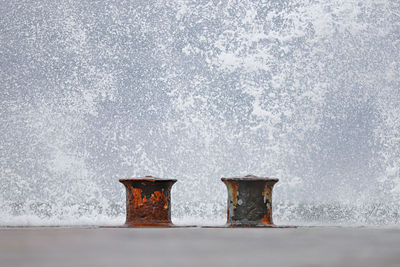 Two rustymooring bollards against waves splashing in the background