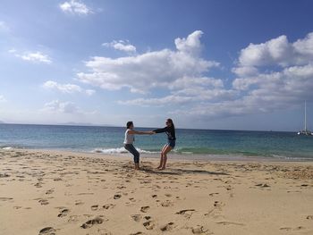 Playful friends on shore at beach against sky