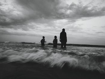 Silhouette friends standing on beach against sky during sunset