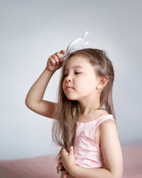 The girl is sitting on the bed and combing her long hair.