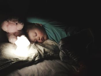 Girl sleeping with teddy bear by illuminated lighting equipment