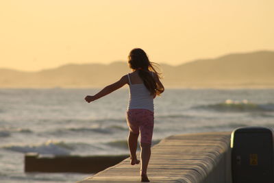 Rear view of girl walking on promenade by sea beach during sunset