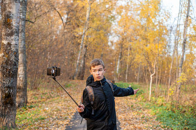 A teenage boy in a black jacket and a monopod in his hand shoots video on a smartphone. boy blogger