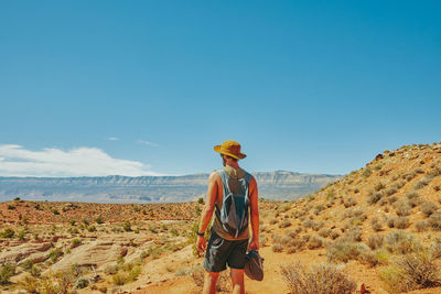 Back of young man wearing hat gazing out to desert during hike.