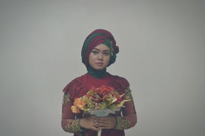 Portrait of young woman holding flower bouquet against white background