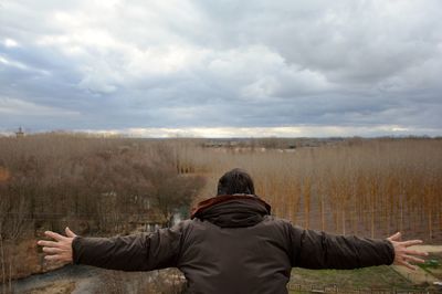Rear view of man with arms outstretched standing against cloudy sky during sunset