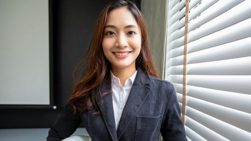 Portrait of young businesswoman standing against window