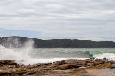 Waves splashing on rocks at shore against sky