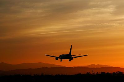 Airplane flying above silhouette landscape at sunset