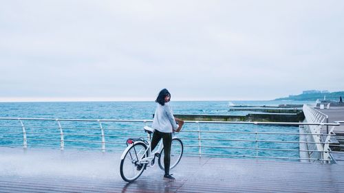 Woman with bicycle standing on promenade against sky