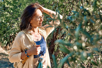 Portrait of woman stending in olive grove, enjoying mountain view, traveling with backpack