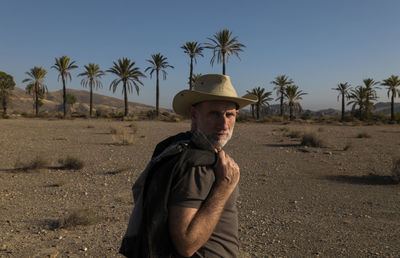 Adult man in cowboy hat on tabernas desert with palm trees against blue sky. almeria, spain