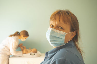 Portrait of woman wearing mask with mother and baby in background