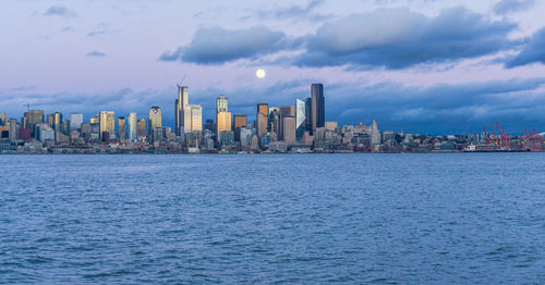 A full moon shines above the seattle skyline.