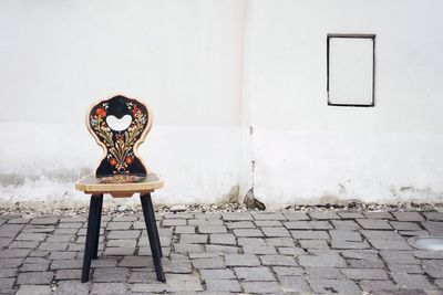 Empty chair on footpath against wall