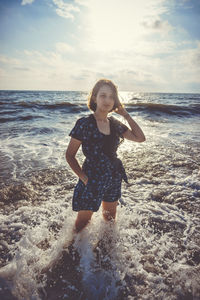 Beautiful young woman standing at seashore against sky