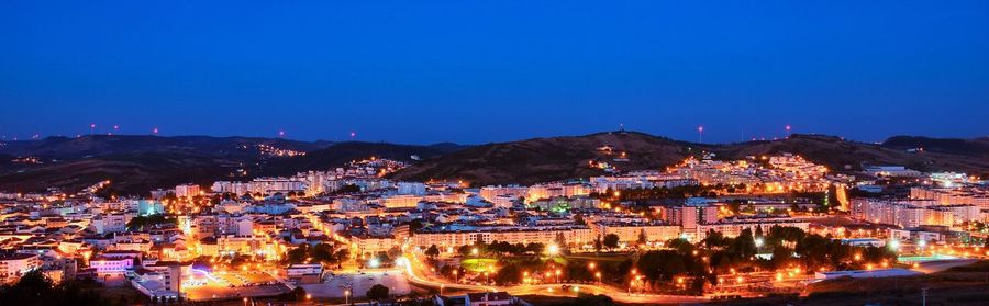 High angle view of illuminated cityscape against blue sky