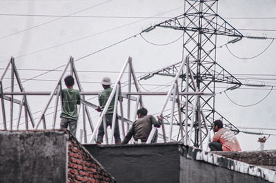 People working on electricity pylon against sky