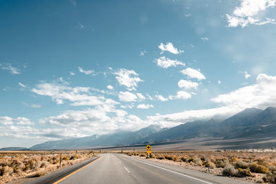 Empty road amidst field by mountain against sky